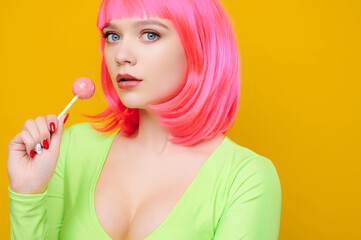 Freaky seductive woman on pink wig and green t-short eat or lick big lollipop on bright yellow background