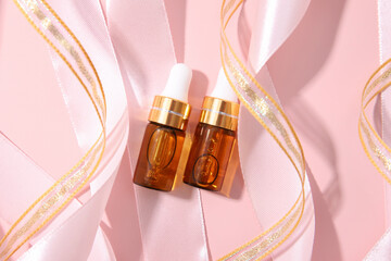 Serum in two glass bottle with pipette and pink ribbons, essential oil cosmetic flat lay, mockup. Skin care, moisturizing beauty product on pink background. Party, New Years day, Christmas. Close up.