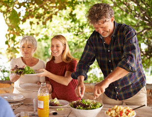 Dads in charge of dishing up. A view of a family preparing to eat lunch together outdoors.