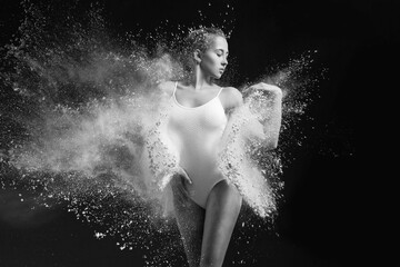 Young beautiful girl in a bodysuit in an explosion of white powder isolated on a dark black background. The concept of energy, power, movement. concept for advertising. Splashes of white paints on a d