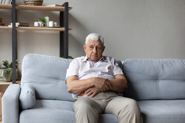 Lonely thoughtful older 75s man sits alone on sofa thinking of loneliness, life or health problems. Melancholic senior lost in sad thoughts looks pensive, recollect past, suffers from solitude concept - obrazy, fototapety, plakaty
