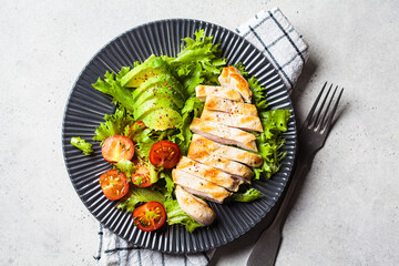 Grilled chicken breast salad with avocado and cherry tomatoes on gray plate. Healthy diet food...