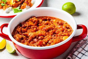 Vegan chili con carne with vegetables and beans in tomato sauce in a red saucepan. Mexican food concept.