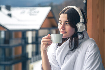 A young woman is listening to music wrapped in a blanket on the balcony.