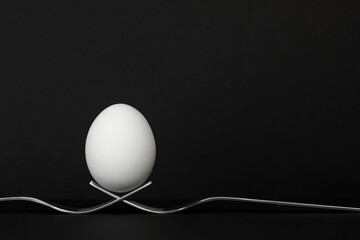 Egg balanced on two metal forks, black background. Easter concept.
