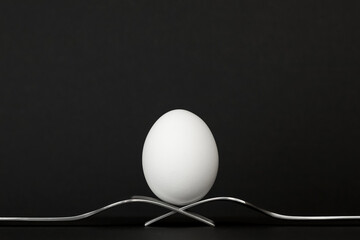 White egg standing on two forks on a black background. Easter concept.