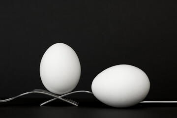 Egg in balance on two forks on black background. Easter concept.