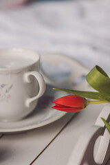 Sill life spring red tulip on a white sheet with wooden tray and cup of coffee in a hand painted cup and saucer	