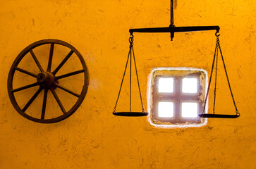 Old wooden wheel and scales on the yellow wall with window.