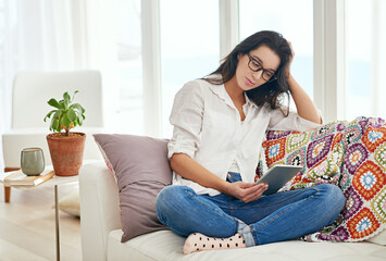 Obraz premium Its just me and my tablet today. Shot of a young woman using a digital tablet while sitting on a sofa at home.