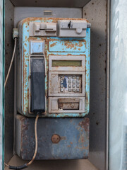 Fototapeta na wymiar Old public telephone on a street in Spain next to the seaside, rusty, decayed and weathered