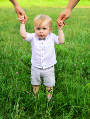 Baby child on the green grass in summer park. Parents hand and child. Perfect family holding hands, adopted child being supported by loving parents.