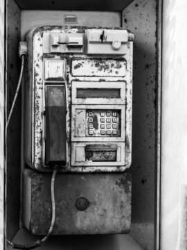 Black and wild image of an old public telephone on a street in Spain next to the seaside, rusty, decayed and weathered