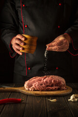 The chef sprinkles raw meat with salt. Preparing fresh meat before roasting. Menu concept for restaurant or hotel. European cuisine