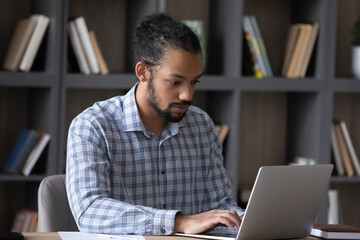 Serious concentrate Black worker guy working on online project at laptop, using professional app, internet service. Student doing research study in college library, sitting at computer alone