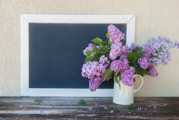 Empty space chalk blackboard with white frame and lilac flowers bouquet