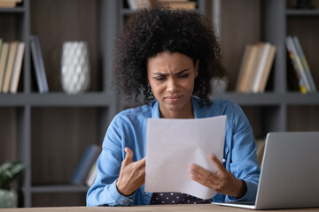 Annoyed frustrated African student girl receiving paper letter, rejection notice from university, feeling stress. Upset young Black employee woman reading document with bad dismissal news.