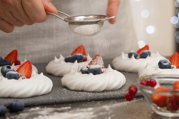 Obraz na płótnie Canvas Hands decorate vanilla meringue with blueberries and strawberries. Food dessert concept
