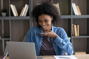 Happy African entrepreneur girl making mobile phone call, talking on speaker, recording audio message for online chat, giving voice command on cellphone to AI virtual assistant