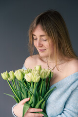 Portrait of a young woman with a bouquet of tulips on a gray background.