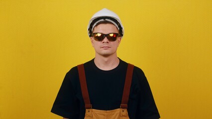 Young guy builder looking at the camera in protective goggles and a hard hat on an isolated background