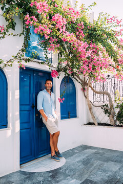 Junger Mann in hellblauen Hemd stehend vor blauer Türe auf Mykonos in Griechenland