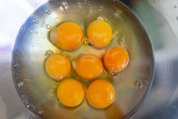 Eggs broken into a metal bowl with unbroken yolks