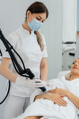 Obraz premium A young girl gets carbon peeling for the skin of her hands in a beauty salon. Laser pulses cleanse the skin. Hardware cosmetology. The process of photothermolysis, warming the skin.