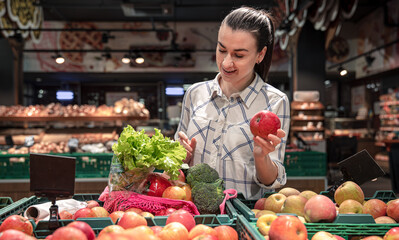 A young woman chooses fruits and vegetables in a supermarket.