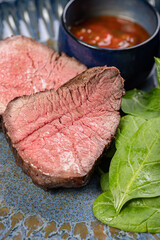 Delicious, Juicy grilled piece of grilled steak with spinach and sauces on a glossy blue plate.