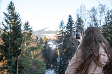 A young woman takes pictures of the mountains on a smartphone.