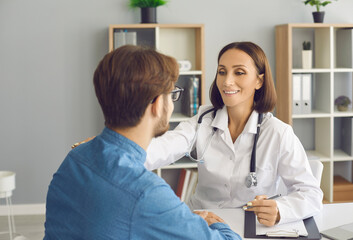 Female doctor having conversation with young man who came to her office. Smiley woman in white lab...