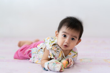 A cute 7 months  smiling asian little baby is laying on the bed with the intravenous infusion set in the pediatric department of the hospital, Concept of sickness and treatment for baby patient.