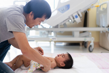 Asian daddy wipe the body of little son to reduce body temperature from fever in the hospital room,...