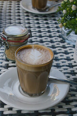 A latte in a glass on a black and white table at an outdoor cafe.
