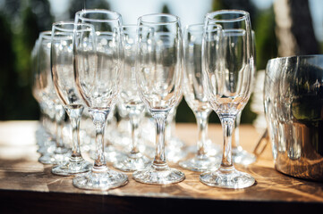 Row of empty champagne glasses on a table outdoors with sun reflection. Selective focus. Celebration concept