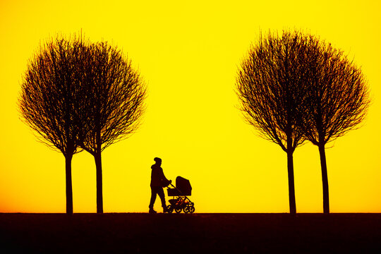 yellow sky tinted with sunset and silhouette of a figure with a stroller