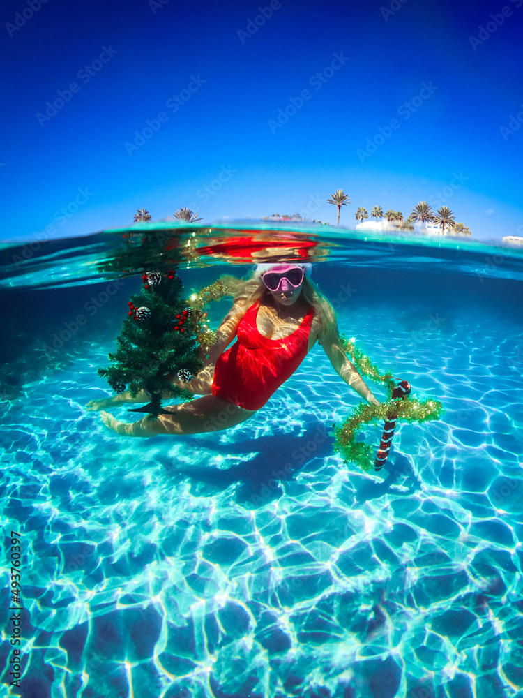 Wall mural Free diver woman in red swimsuit with Christmas tree, underwater, Freediving underwater in ocean