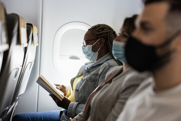African senior woman reading a book traveling on airplane during coronavirus outbreak - Focus on left face