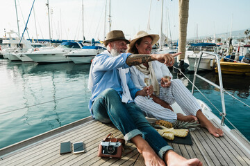 Senior couple drinking champagne on sailboat during summer vacation - Focus on faces