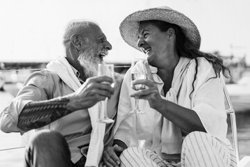 Senior couple cheering with champagne on boat during summer vacation - Focus on right woman face -...