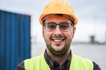 Happy young man smiling on camera working at freight terminal port on background - Focus on face