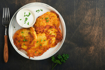 Potato pancakes. Fried homemade potato pancakes or latkes with cream and green onions in rustic plate on old wooden black table background. Rustic style. Healthy food. Top view.