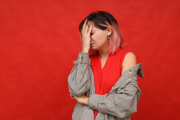 The upset girl covered her face with her hand while standing on a red background