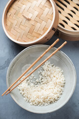 Plate of steamed white rice on a grey concrete background with a bamboo steamer, high angle view, vertical shot