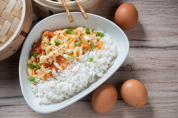 Tomato egg-stir fry with steamed rice served in a grey bowl, high angle view on a brown wooden background