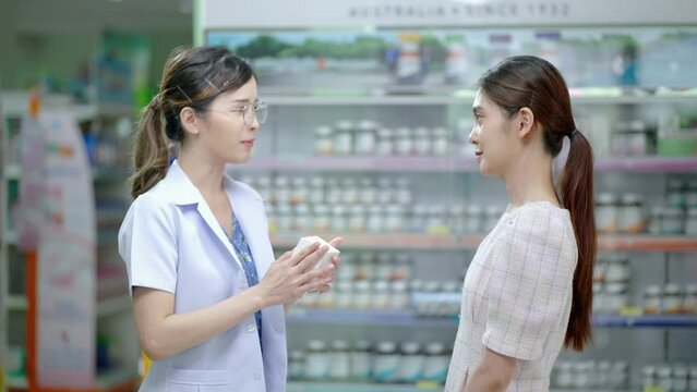 Asian female pharmacist explaining the medicinal properties on the pillbox to a patient or customer according to the doctor's prescription and providing customers with e-service payment at the custome