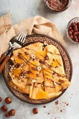 Crepes suzette with oranges and chocolate. Thin crepes with chocolate spread, hazelnuts and orange slices fruit in plate for breakfast on old concrete rustic table background. Copy space. Top view