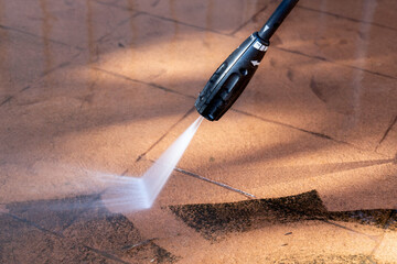 Cleaning dirty backyard paving tiles with pressure washer cleaner.