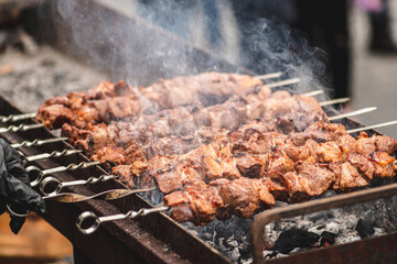 Pork meat skewer, grilled or roasted in a barbecue on an open fire and flames, shashlik or shashlyk for a picnic with pitchforks, close up